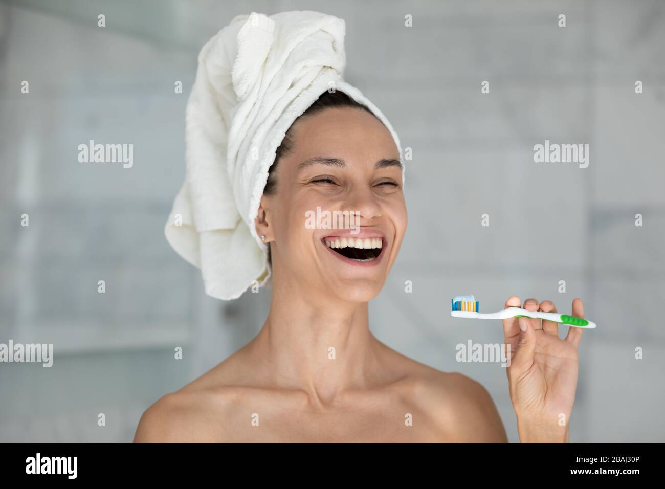 Tête de rire de la femme avec une serviette sur la tête tenant la brosse à dents Banque D'Images