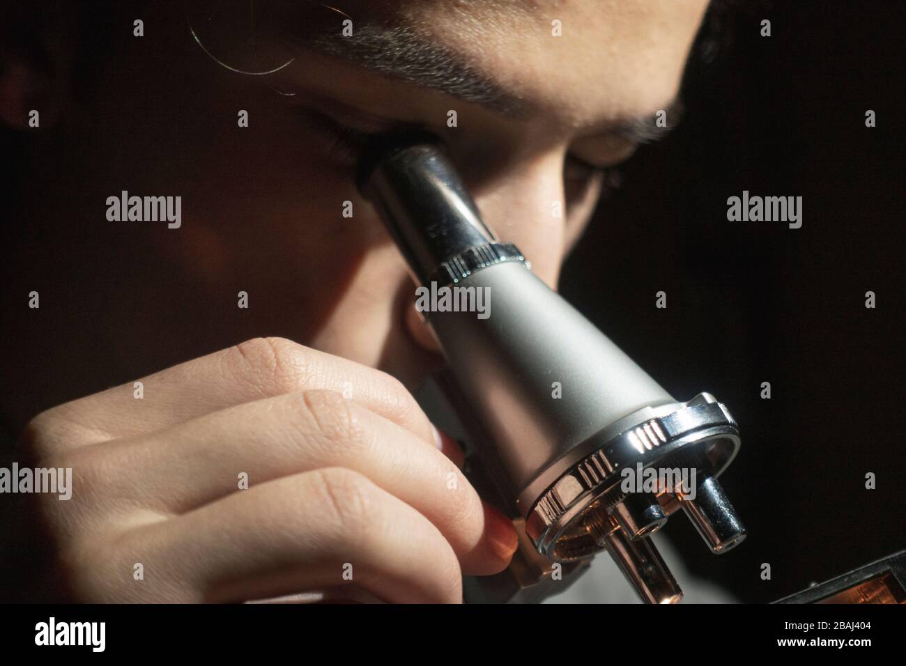 Jeune étudiant en sciences faisant de la recherche regardant par son microscope tard dans la nuit à sa maison Banque D'Images