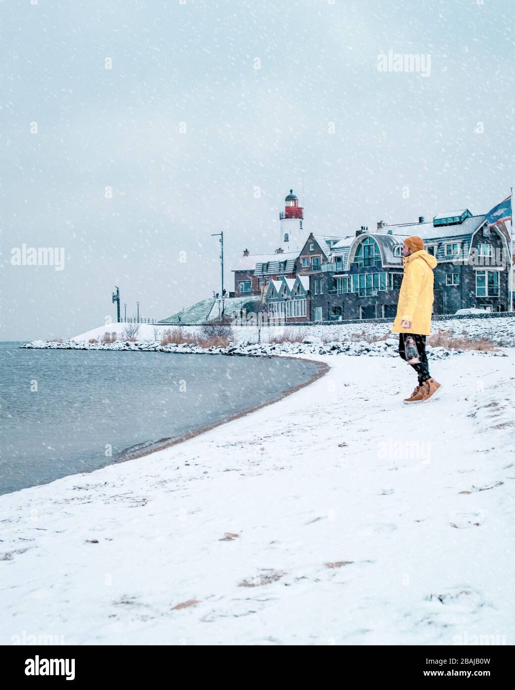 Jeunes hommes en veste de pluie jaune marchant sur une plage enneigée près du phare d'Urk Pays-Bas, hommes avec lampe à huile et manteau de ranin Banque D'Images