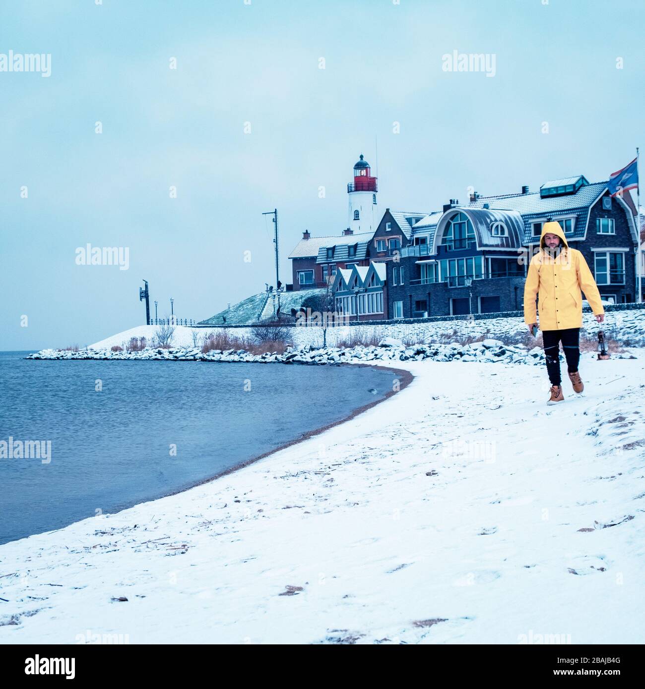 Jeunes hommes en veste de pluie jaune marchant sur une plage enneigée près du phare d'Urk Pays-Bas, hommes avec lampe à huile et manteau de ranin Banque D'Images