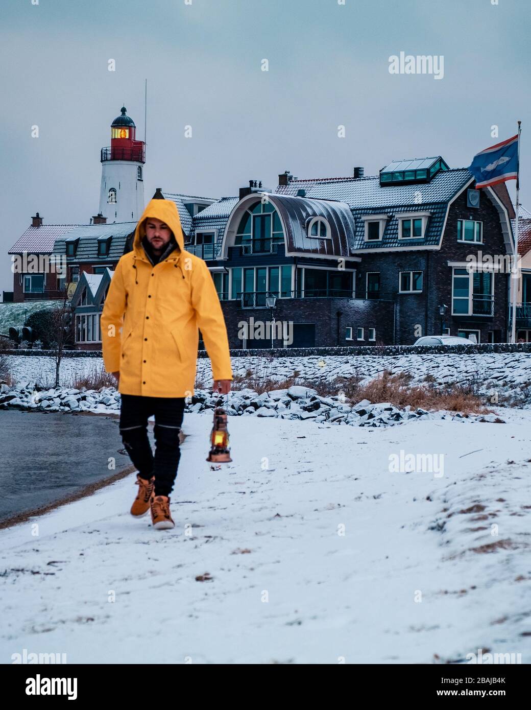 Jeunes hommes en veste de pluie jaune marchant sur une plage enneigée près du phare d'Urk Pays-Bas, hommes avec lampe à huile et manteau de ranin Banque D'Images