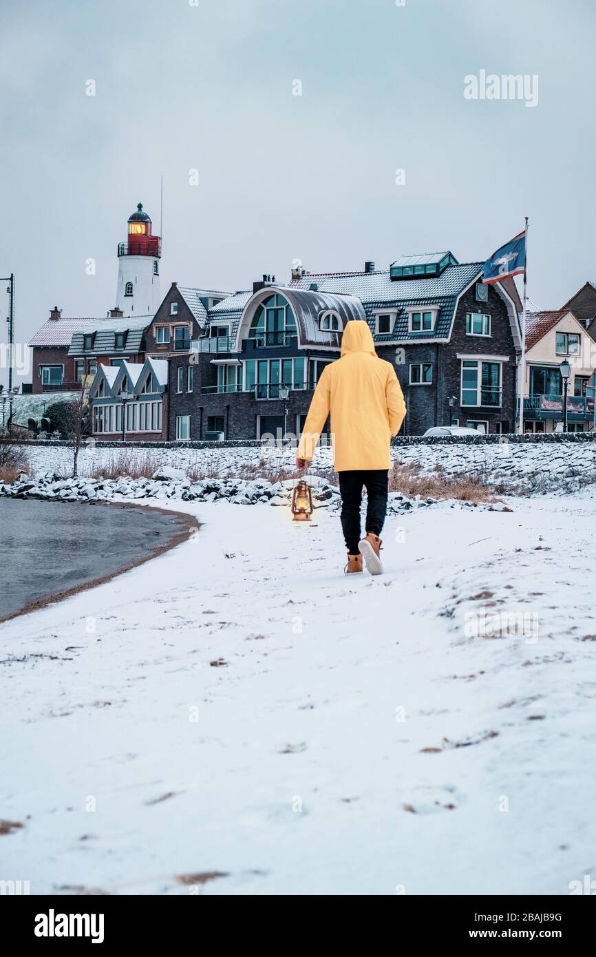 Jeunes hommes en veste de pluie jaune marchant sur une plage enneigée près du phare d'Urk Pays-Bas, hommes avec lampe à huile et manteau de ranin Banque D'Images