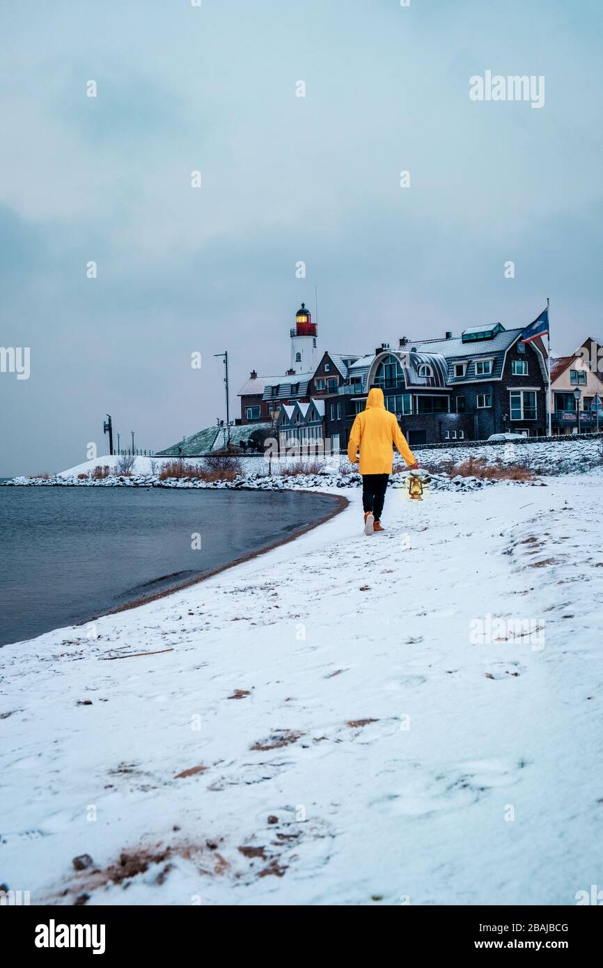 Jeunes hommes en veste de pluie jaune marchant sur une plage enneigée près du phare d'Urk Pays-Bas, hommes avec lampe à huile et manteau de ranin Banque D'Images