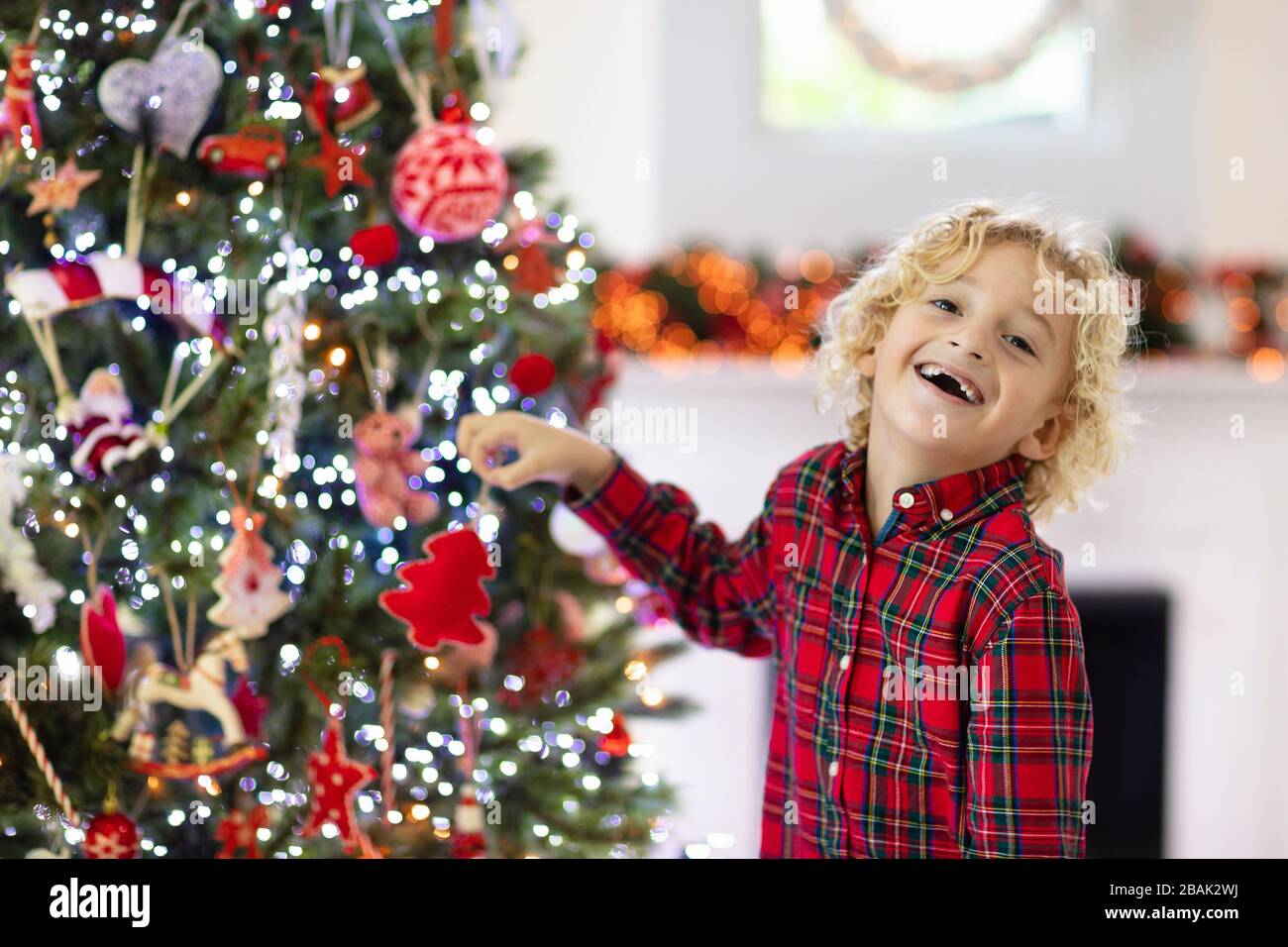 Enfant decorant arbre de Noel a la maison. Petit garcon dans une chemise a carreaux avec ornement de Noel. La famille avec les enfants celebrent les vacances d hiver. Les enfants decorent le