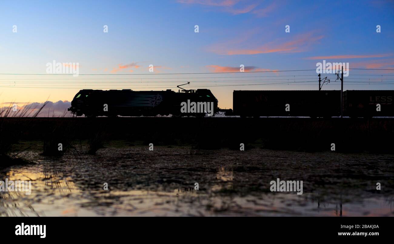 Services ferroviaires directs locomotive électrique Stadler classe 88 transportant un train à conteneurs intermodal sur la ligne principale de la côte ouest, pour une silhouette de coucher de soleil Banque D'Images