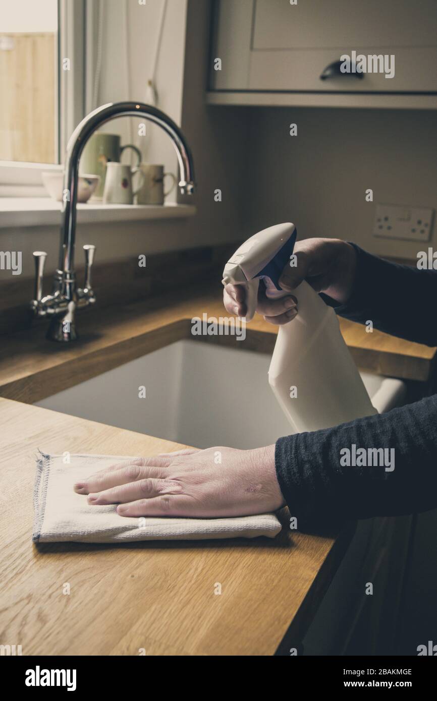 Un gros plan d'une paire de mains humaines nettoyant l'intérieur d'une cuisine avec un spray antibactérien et un chiffon pour désinfecter les surfaces de travail pendant le Cor Banque D'Images