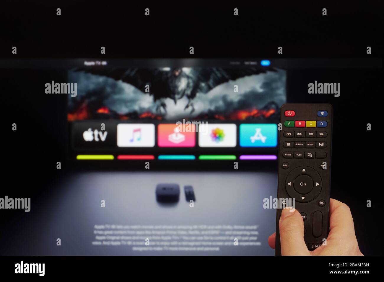 Concept de fournisseur de contenu VOD Apple Streaming Service. La main tient une télécommande multimédia avant un écran avec Apple TV et une page de montre en ligne d'application. Banque D'Images