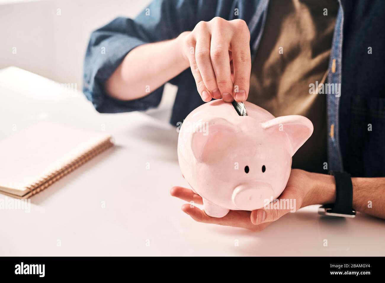 Gros plan sur un homme méconnaissable assis à la table et mettant des pièces dans la piggybank tout en économisant de l'argent en crise Banque D'Images