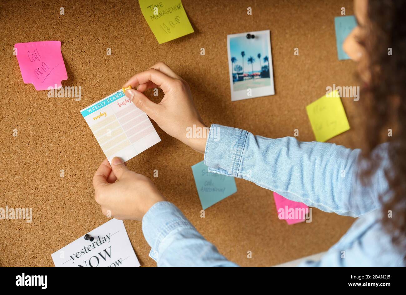 Femme africaine épingler un autocollant de planification hebdomadaire sur le tableau d'humeur au bureau à domicile. Banque D'Images