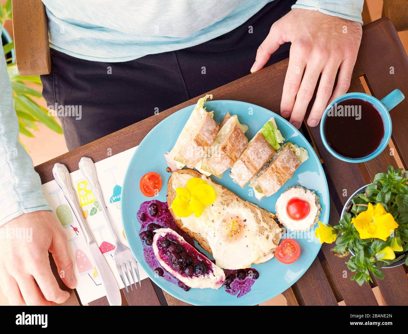 Magnifique cadre coloré de petit déjeuner de printemps avec une variété de nourriture sur une table en bois avec des fleurs et une main d'homme, vue d'en haut. Banque D'Images