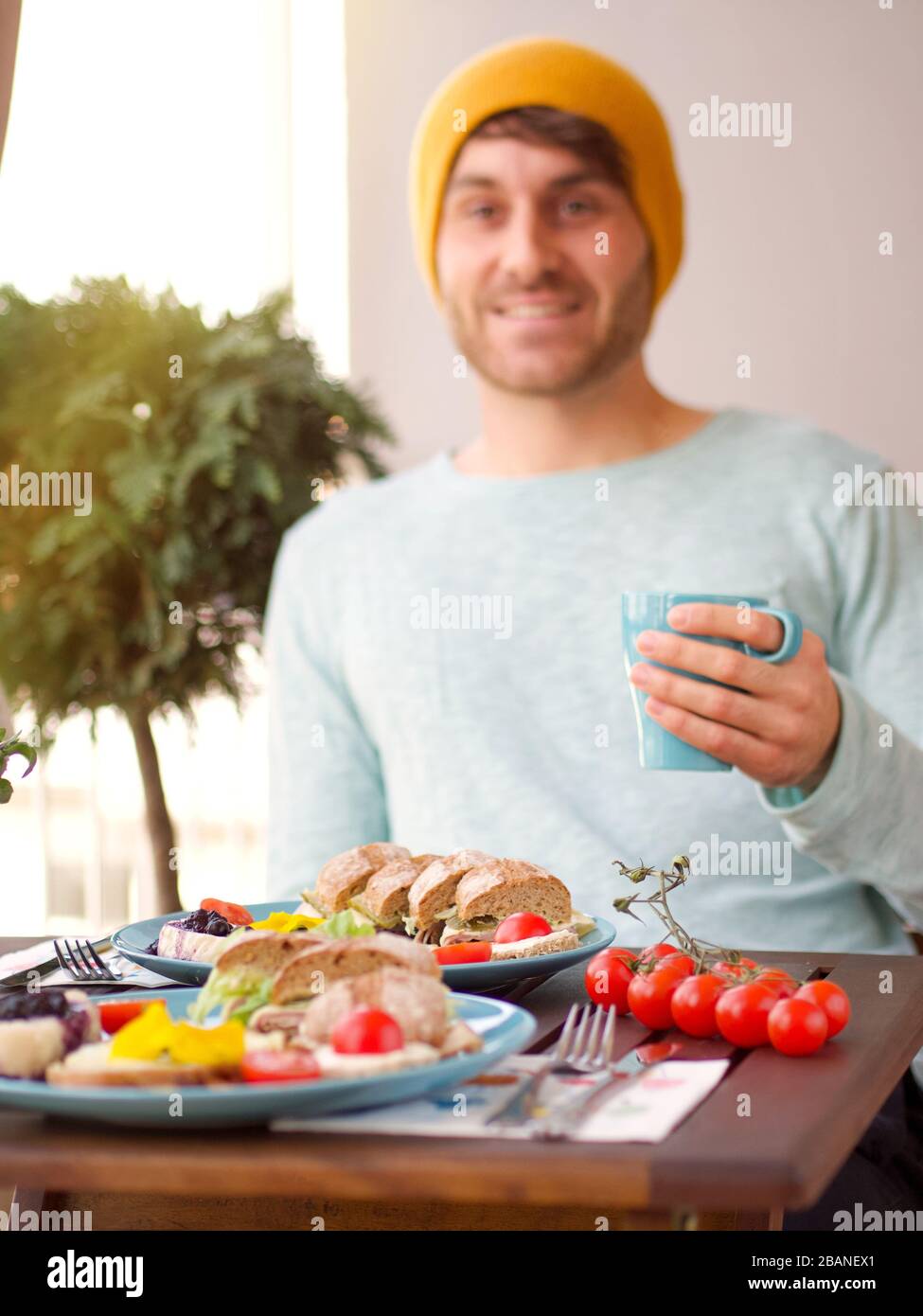 Magnifique cadre coloré de petit déjeuner de printemps avec une variété de nourriture sur une table en bois avec des fleurs une journée ensoleillée et l'homme assis dans le balcon. Banque D'Images
