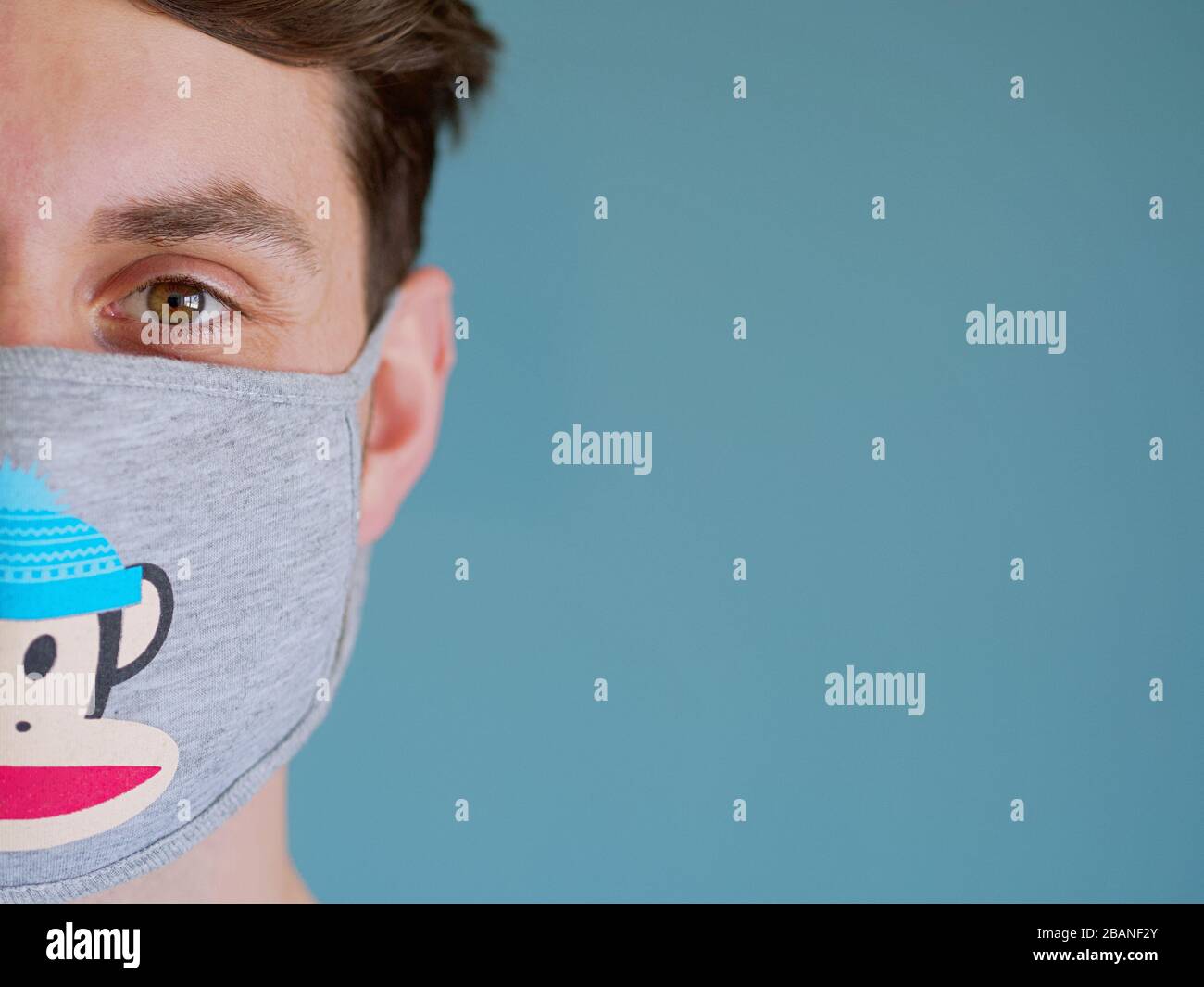 Gros plan d'un homme caucasien portant un drôle de masque de protection du visage de singe avec des yeux et des cheveux bruns, depuis la nouvelle éclosion de coronavirus. Banque D'Images