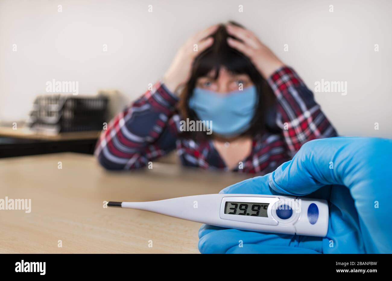 Éclosion de pandémie de Covid-19. Forte fièvre sur le thermomètre médical électronique dans la main infirmière dans le gant bleu. Femme malade avec masque bleu dans le cabinet du médecin. Banque D'Images