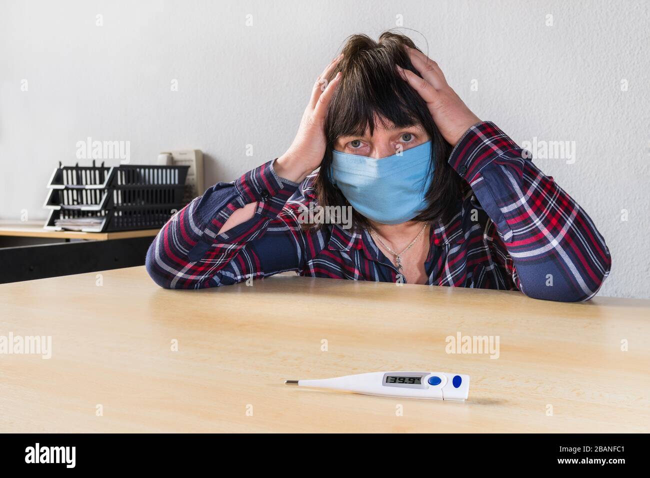 Femme malade atteinte de coronavirus et masque de protection bleu sur le visage. Éclosion de pandémie de Covid-19. Fièvre sur thermomètre médical. Maux de tête en quarantaine. Banque D'Images