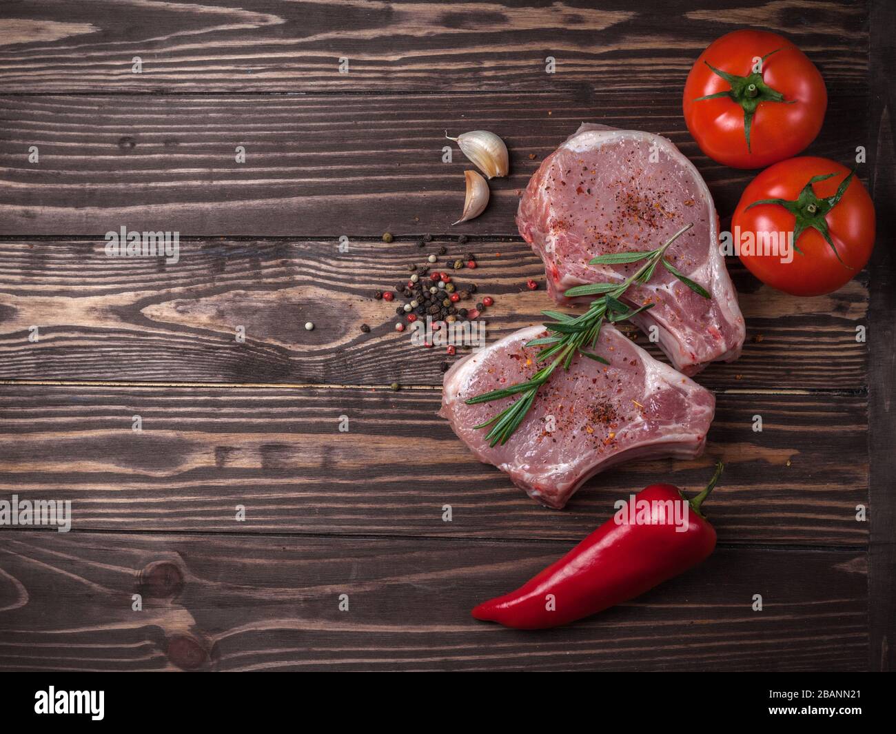 Bifteck de porc haché avec épices vue de dessus. Viande crue, tomate, poivron rouge et poivre sur un plan d'examen en bois Banque D'Images