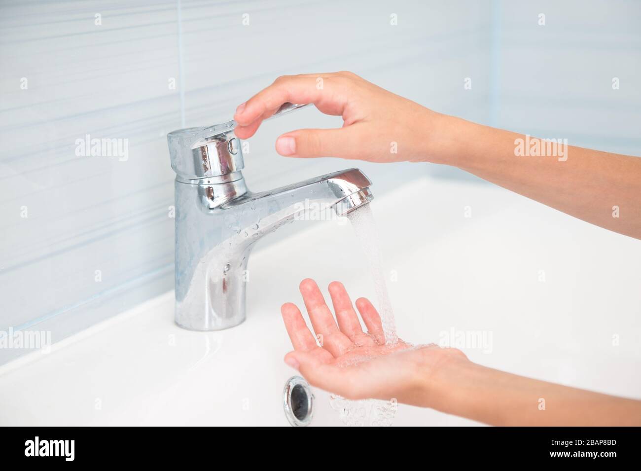 petit enfant, petites mains ouvrant robinet avec de l'eau qui coule dans la salle de bains Banque D'Images