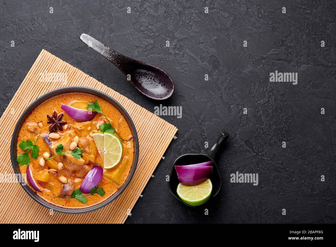 Un curry de massaman de poulet dans un bol noir sur fond d'ardoise sombre. Massaman Curry est un plat de cuisine thaïlandaise avec de la viande de poulet, de la pomme de terre, de l'oignon et de nombreuses épices. Banque D'Images