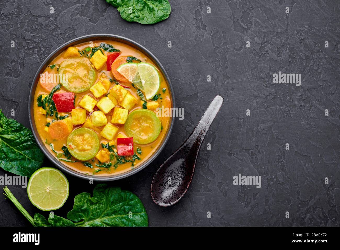 Veau jaune curry thaïlandais avec tofu et légumes dans un bol noir sur fond d'ardoise sombre. Curry thaïlandais végétarien avec tofu, courgettes, poivre, épinards, voiture Banque D'Images