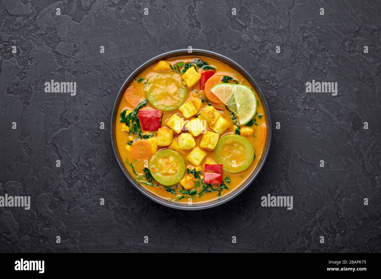 Veau jaune curry thaïlandais avec tofu et légumes dans un bol noir sur fond d'ardoise sombre. Curry thaïlandais végétarien avec tofu, courgettes, poivre, épinards, voiture Banque D'Images