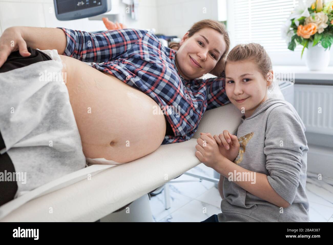 Bonne fille de pré-adolescence assis près de sa mère enceinte avec grand ventre dans la salle d'échographie Banque D'Images