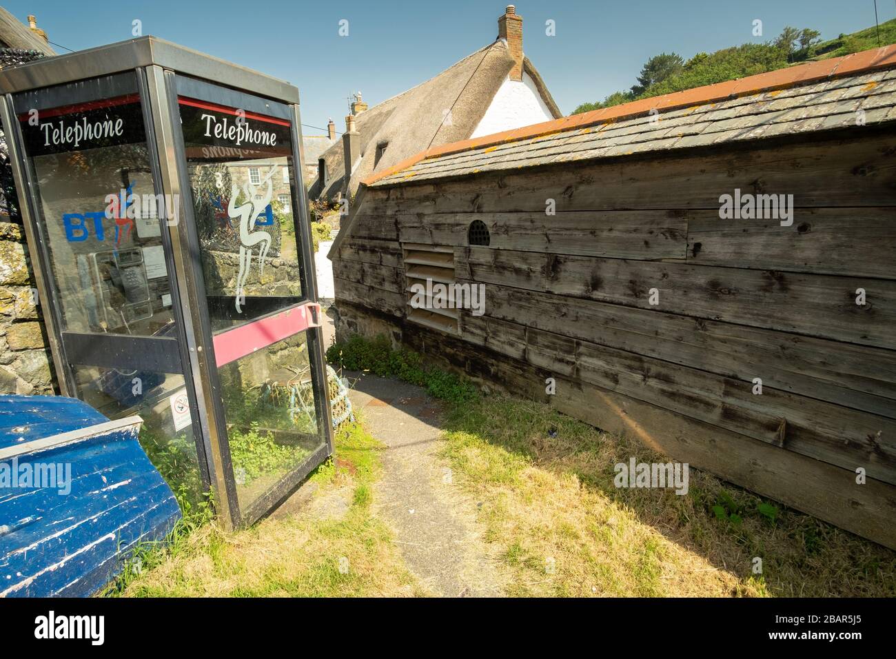 Vide boîte de téléphone BT à côté du sentier, bateau et homard pot avec vieux mur en bois dans le petit village de pêche pittoresque de Cadgwith, Cornwall, Angleterre Banque D'Images