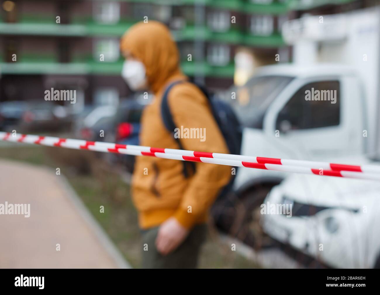 Homme flou dans une capuche et masque de protection derrière une clôture en ruban sur la rue. Restez à la maison. Coronavirus ou covid 19 quarantaine. Banque D'Images