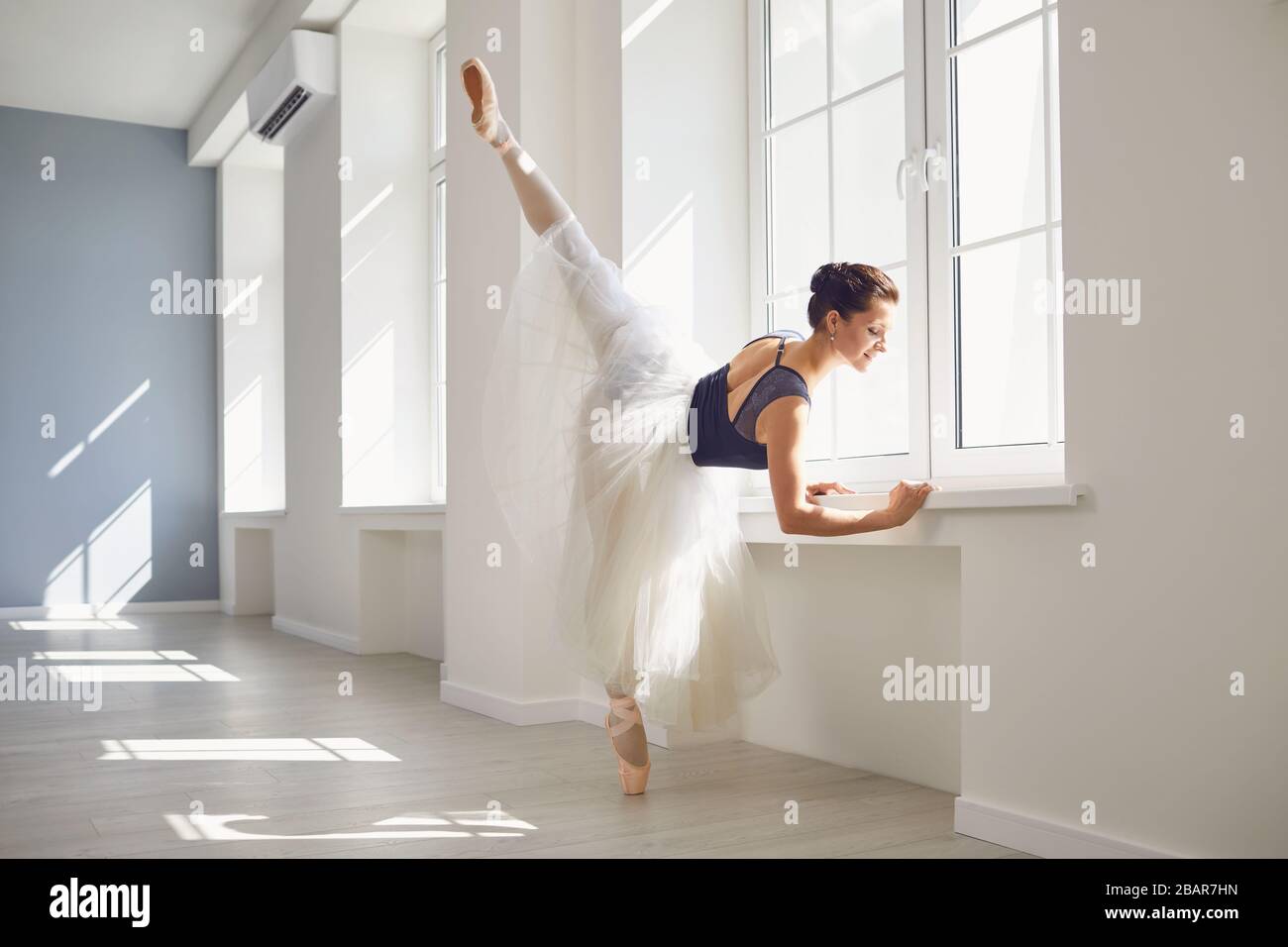 Ballerine. La jeune danseuse de ballet élégante répète une performance dans un studio blanc avec des fenêtres. Banque D'Images
