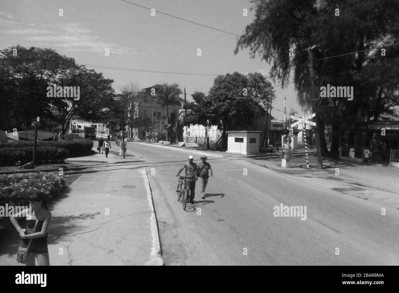 Vélo pousser la voie ferrée personnes marcher marcher temps chaud les arbres traversent les routes signes à l'extérieur des hommes homme chemin de la route maisons architecture Cuba Banque D'Images