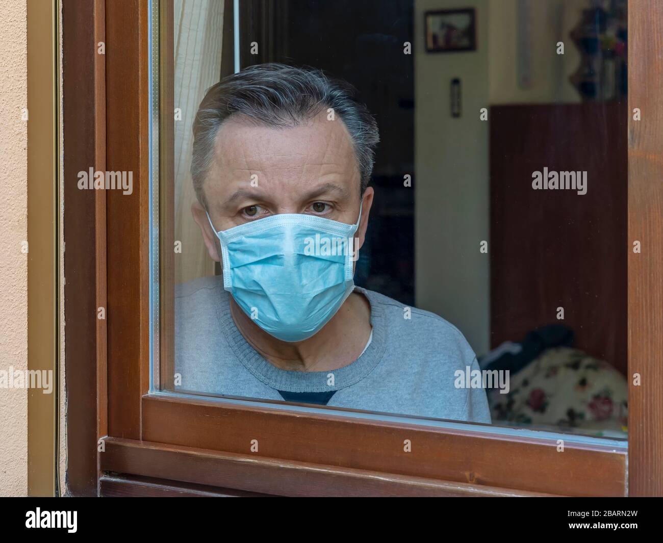 Homme italien avec masque de protection, forcé de rester à la maison en raison du coronavirus covid-19, disconsolate regarde la fenêtre de la maison Banque D'Images