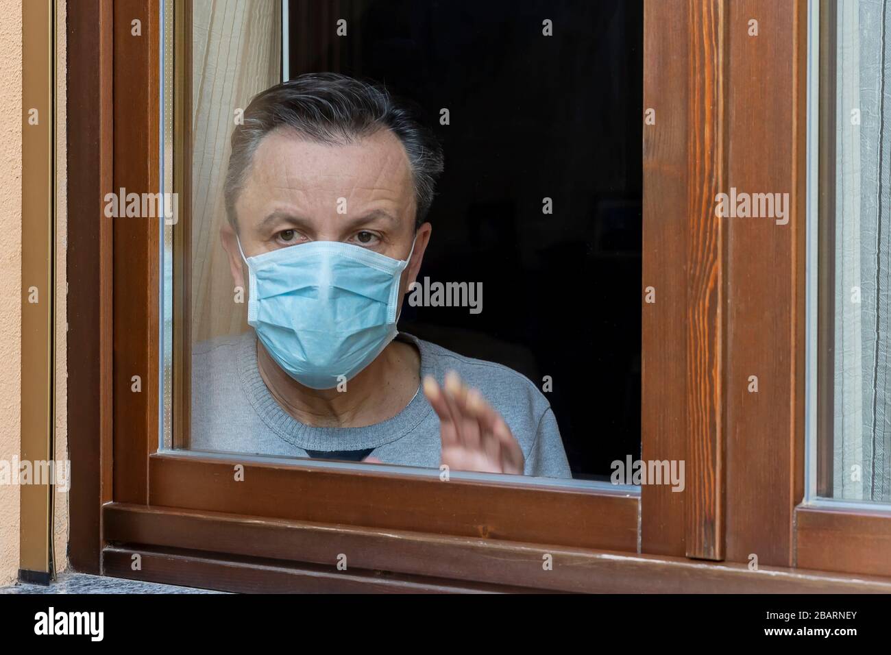 Homme italien avec masque de protection, forcé de rester à la maison en raison du coronavirus covid-19, disconsolate regarde la fenêtre de la maison Banque D'Images