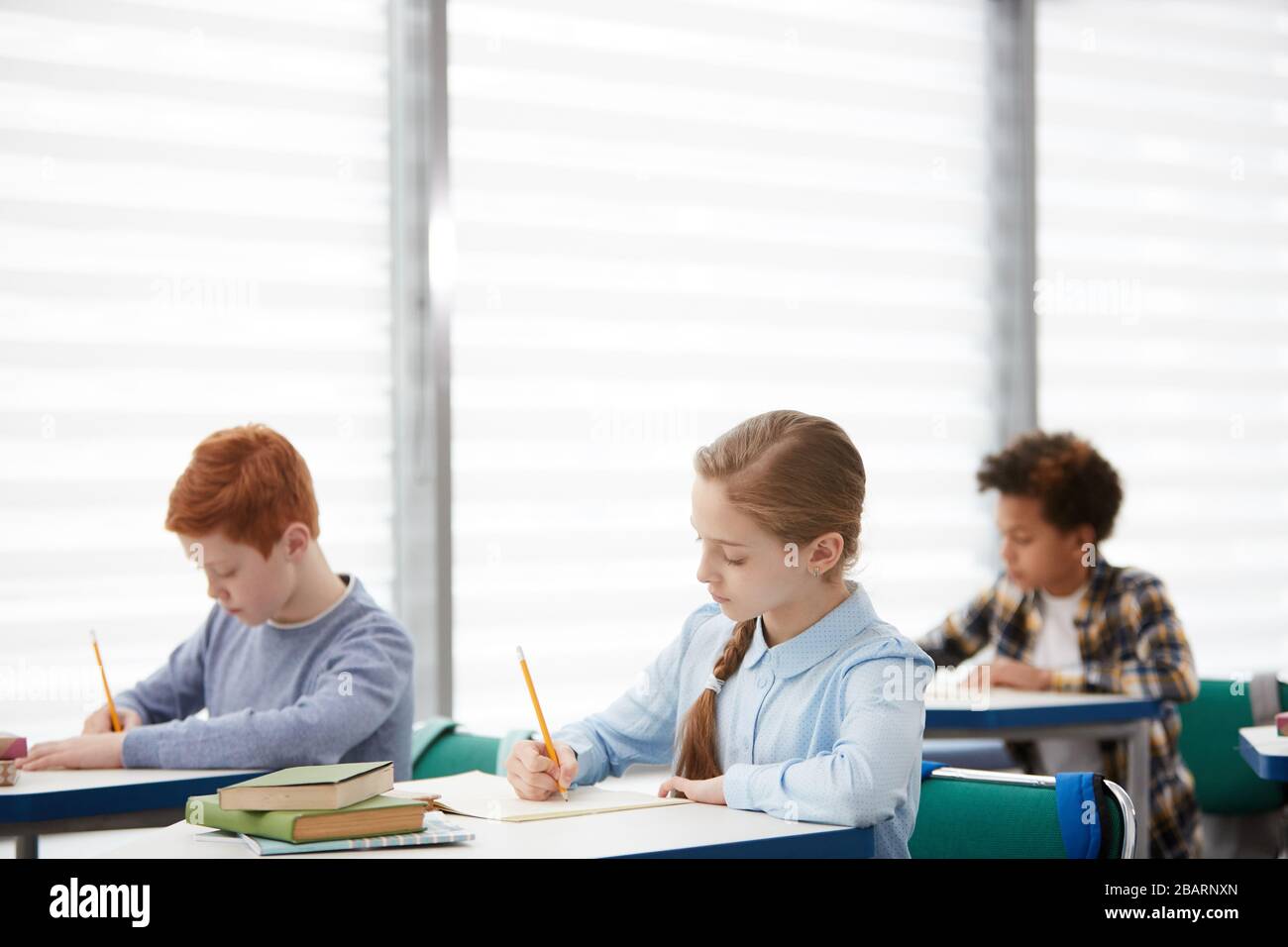 Vue latérale d'un groupe multi-ethnique d'enfants assis sur un bureau à l'école et écrivant des notes d'essai, espace de copie Banque D'Images