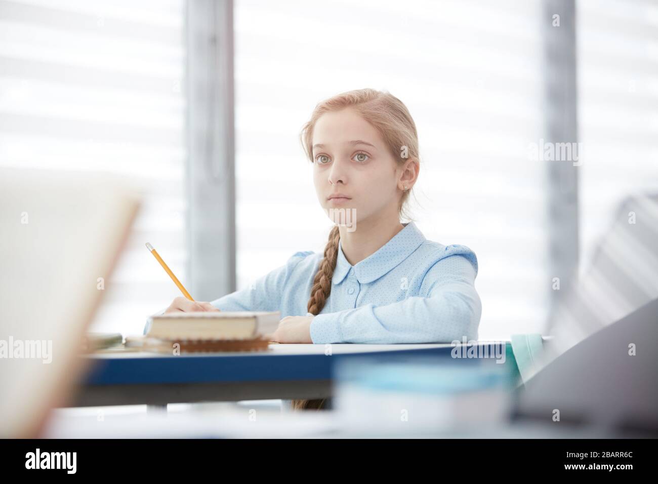 Portrait d'une jolie écolière blonde assise au bureau en classe scolaire et à l'écoute du professeur, espace de copie Banque D'Images