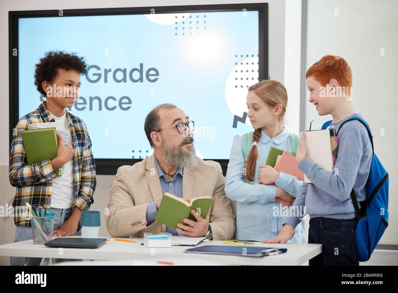 Groupe multi-ethnique d'enfants debout autour de l'enseignant supérieur barbu dans la classe scolaire, espace de copie Banque D'Images