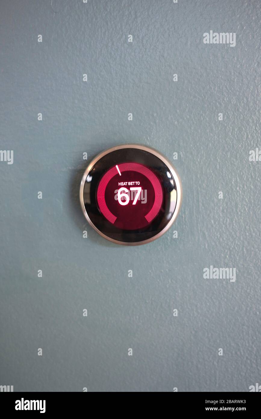 thermostat d'ambiance intelligent avec centre rouge en mode chauffage. Économie d'énergie chauffage maison. Produit isolé sur paroi bleue Banque D'Images