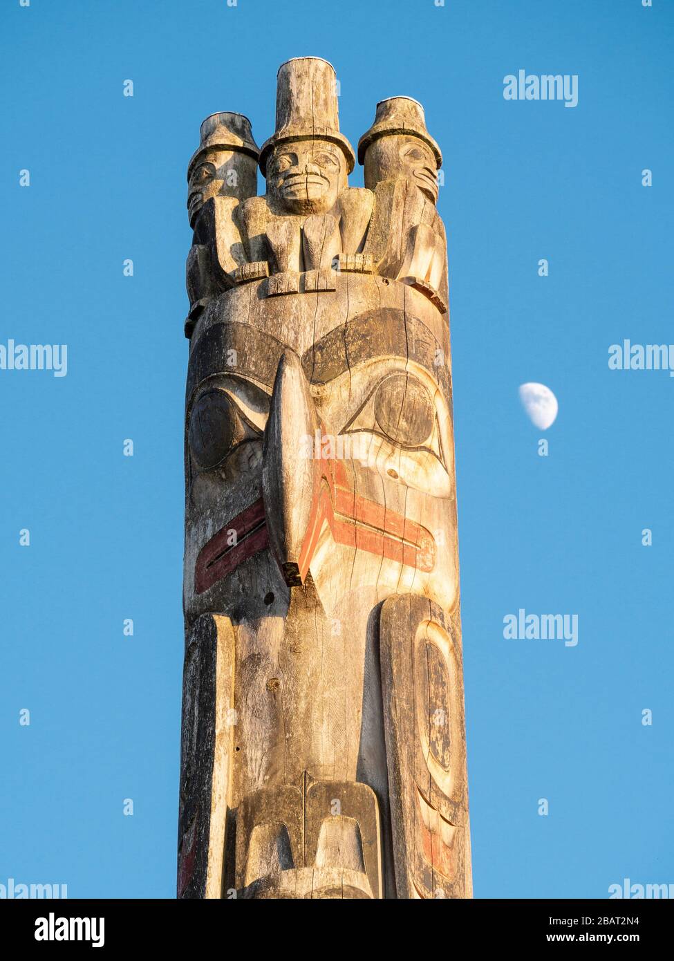 Totem Pole au coucher du soleil et lever de lune : le sommet d'un grand totem sculpté de la côte ouest exposé au Musée d'anthropologie de l'UBC contre un ciel bleu. Banque D'Images