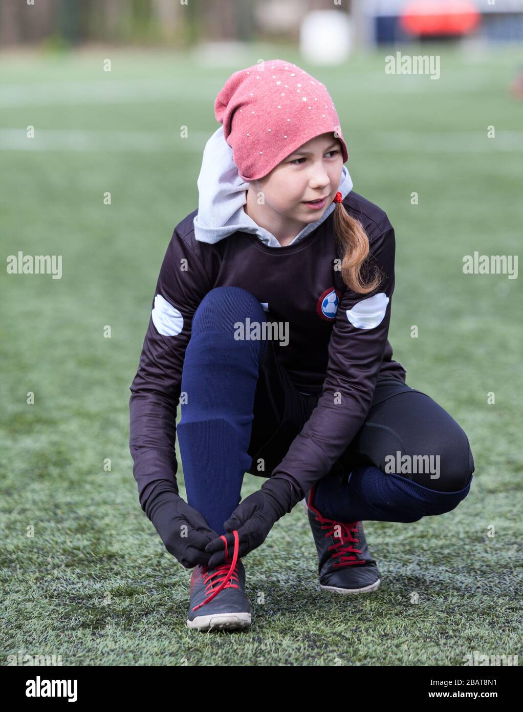 Un joueur de football caucasien de onze ans fait des lacets de ficelage sur des crampons, terrain vert artificiel Banque D'Images