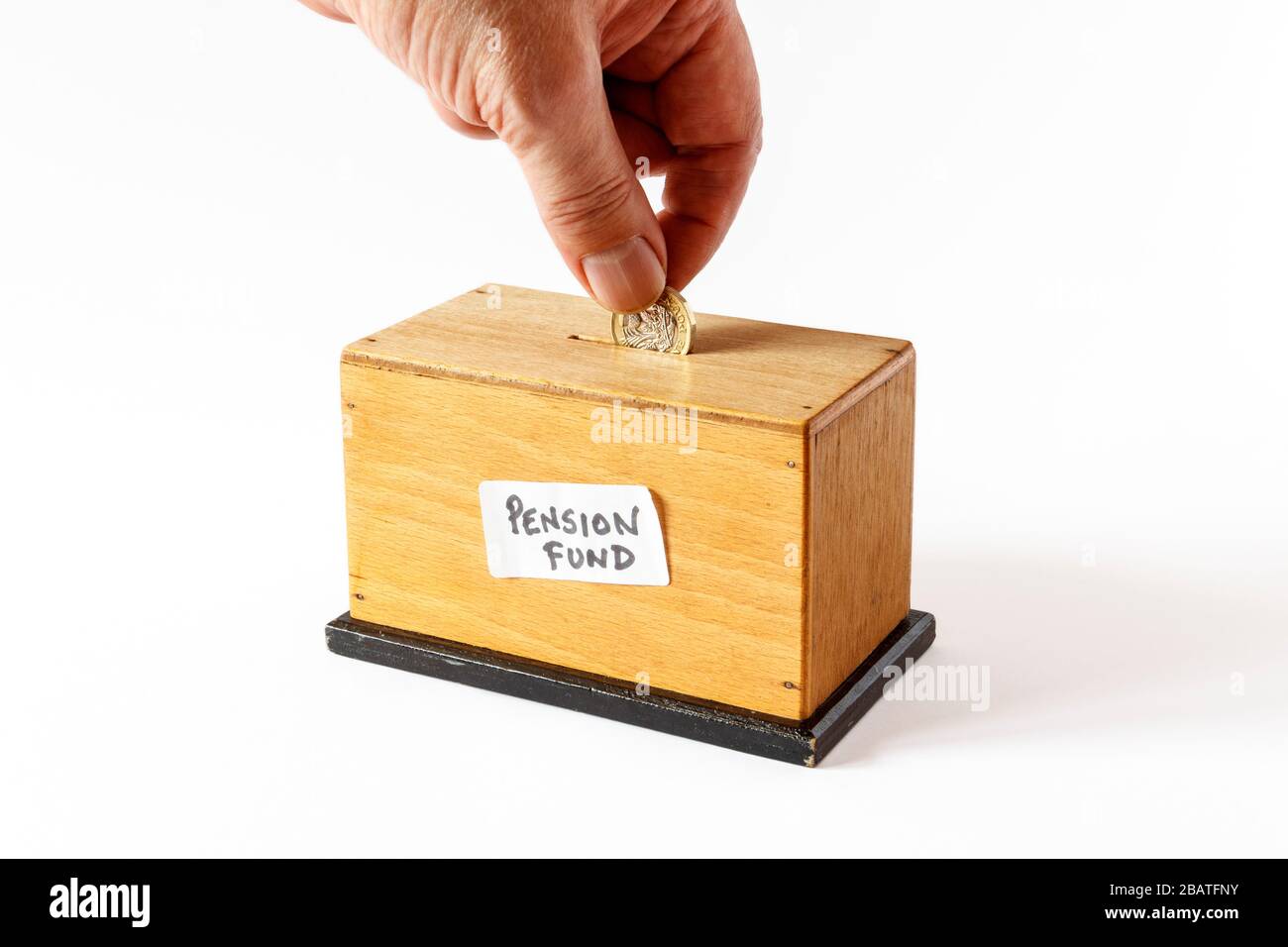 Une caisse en bois faite maison avec une étiquette manuscrite "caisse de retraite", une main masculine insérant une pièce de 1 £ Banque D'Images