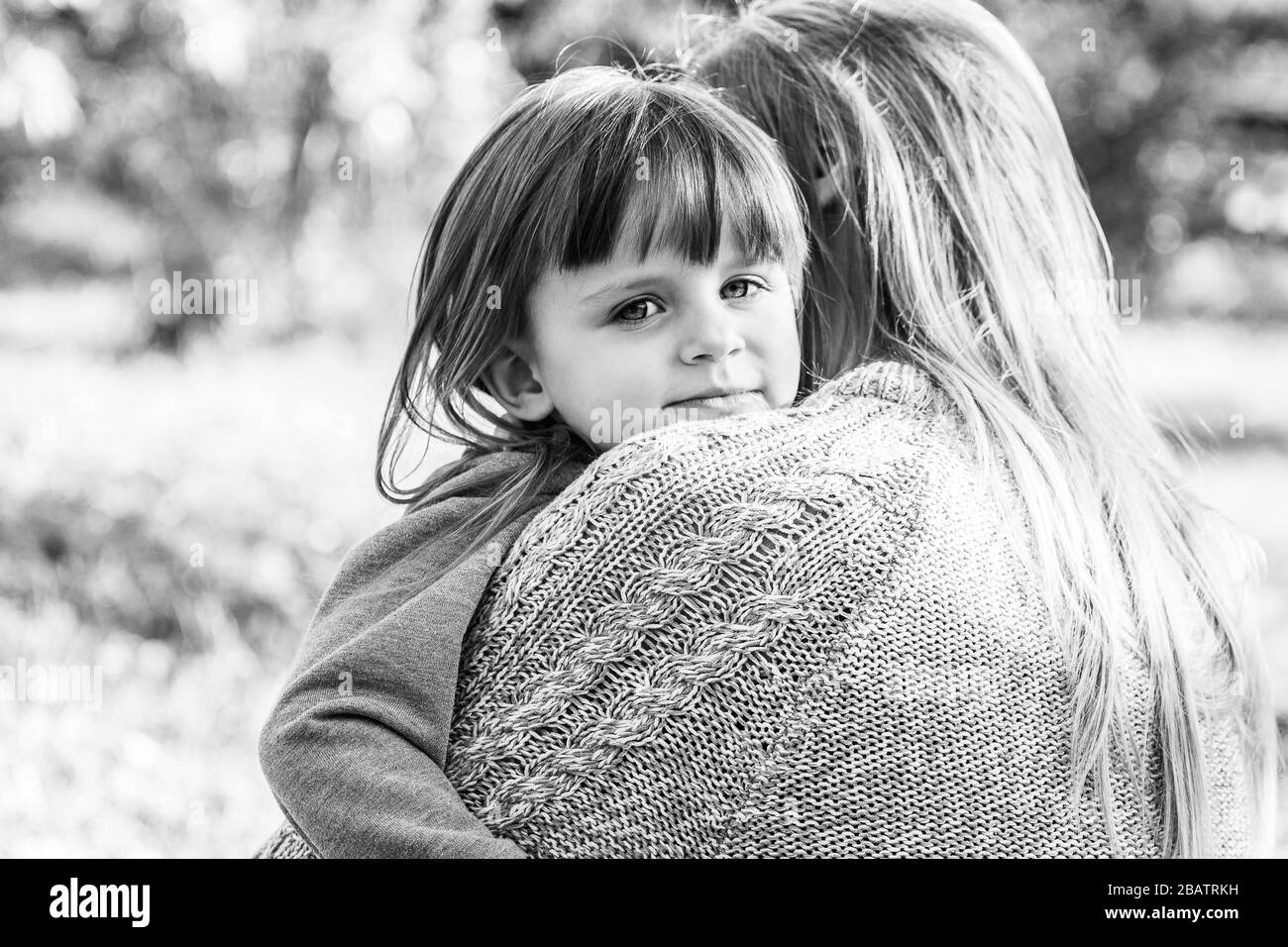 Photo en noir et blanc de la jeune belle femme calmant et embrassant sa fille triste tout en se tenant dehors. Petite fille déçue l'embrassant Banque D'Images