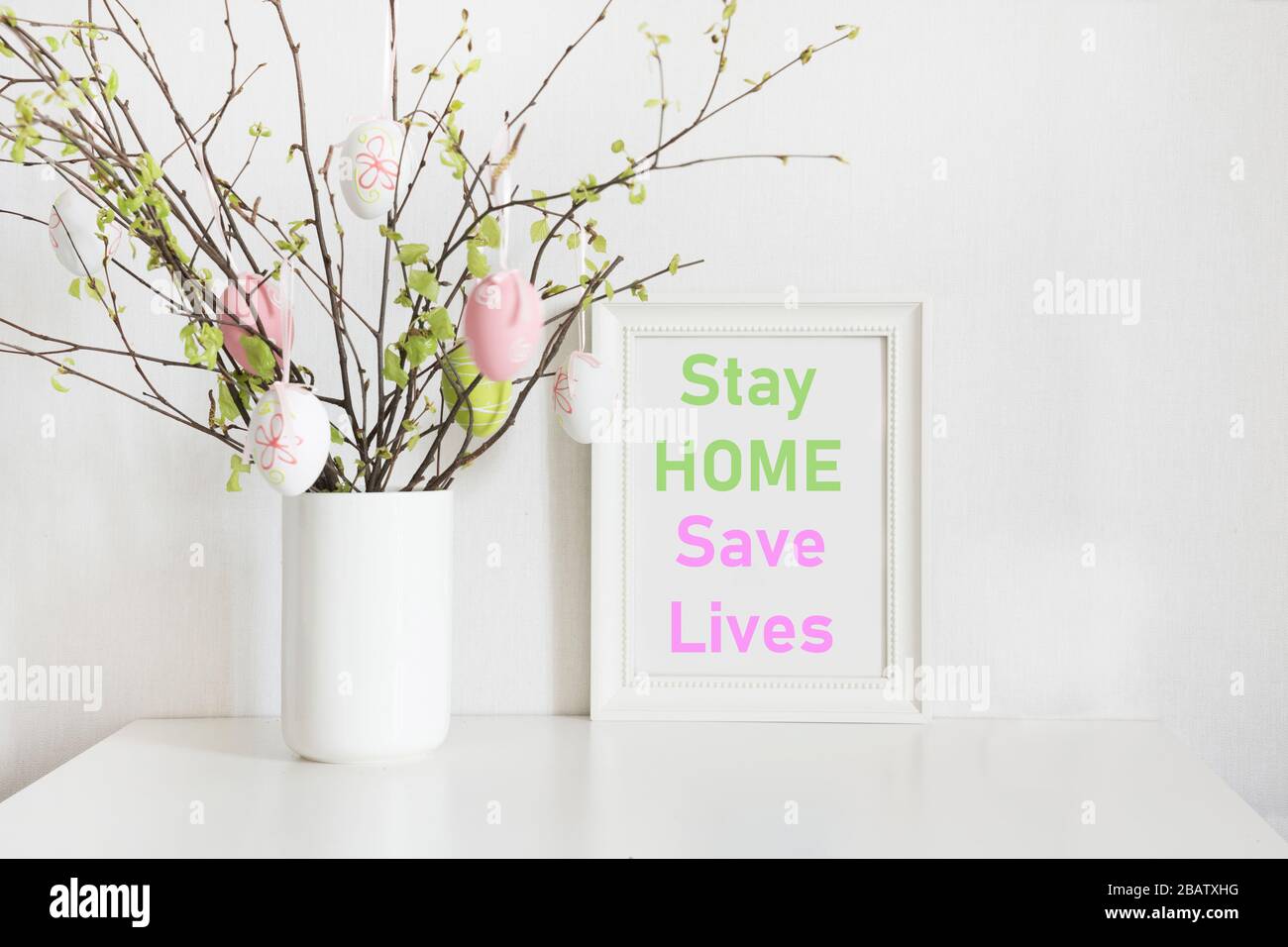Concept de Pâques 2020. Vase avec branches de bouleau avec œufs pastel et cadre pour oeufs de Pâques et cadre avec slogan - rester à la maison, sauver des vies. Banque D'Images