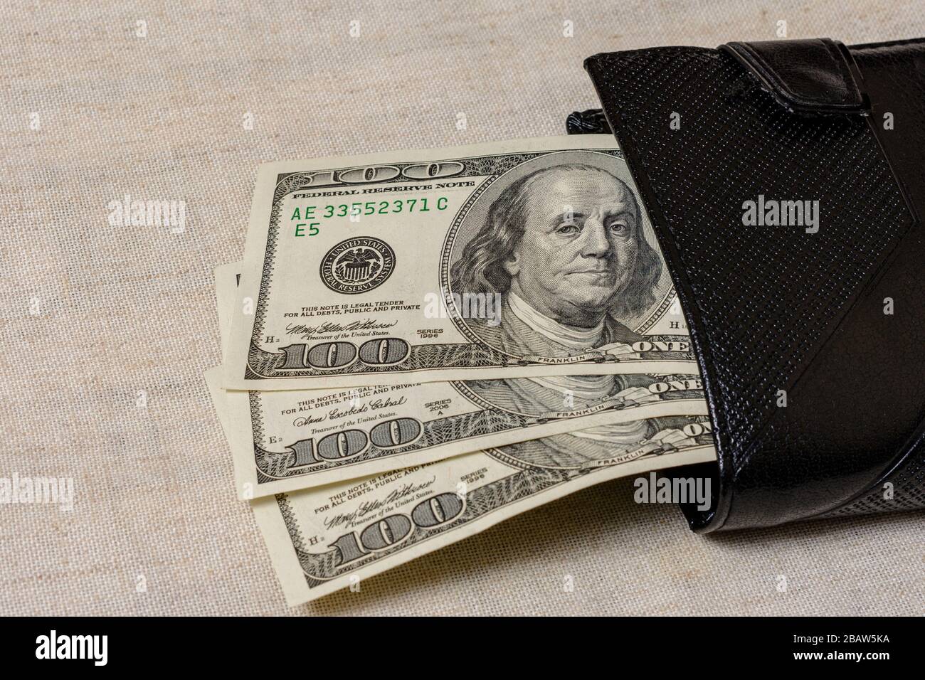 Cent dollars se trouvent dans un sac à main noir sur fond gris. Banque D'Images