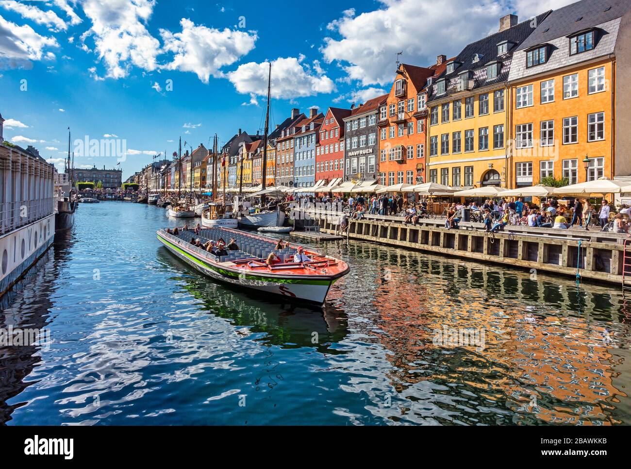 Bateau de tourisme sur le canal partant de Nyhavn dans le port de Copenhague Danemark avec les restaurants pleins de clients en début de soirée ensoleillée. Banque D'Images
