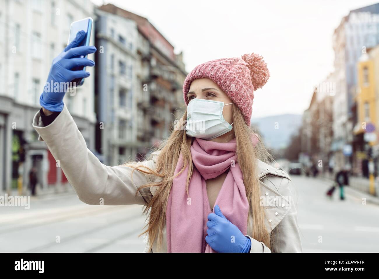 Femme avec masque médical et gants prenant selfie dans la ville de verrouillage Banque D'Images