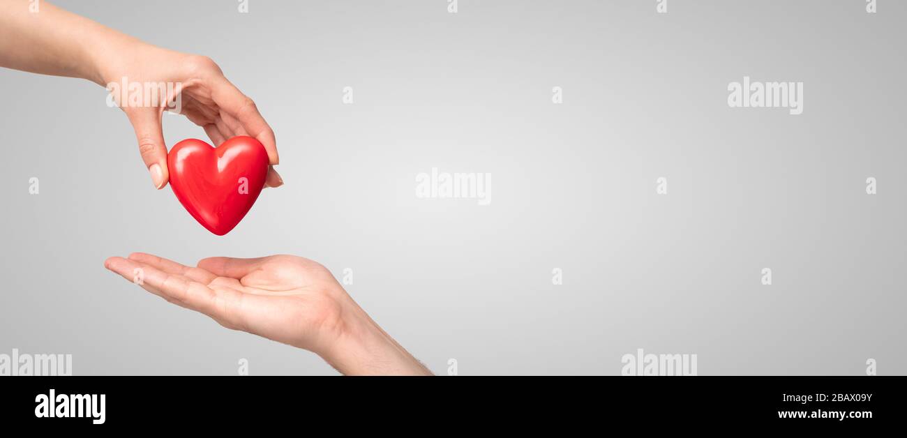 Le concept de charité, d'amour, de don et de main d'aide. Journée internationale de cardiologie. Une femme donne un cœur rouge aux mains de l'homme. Banque D'Images