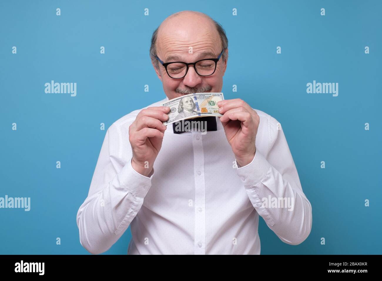 Un homme caucasien senior en lunettes tient un billet de banque et de dollar sniff Banque D'Images