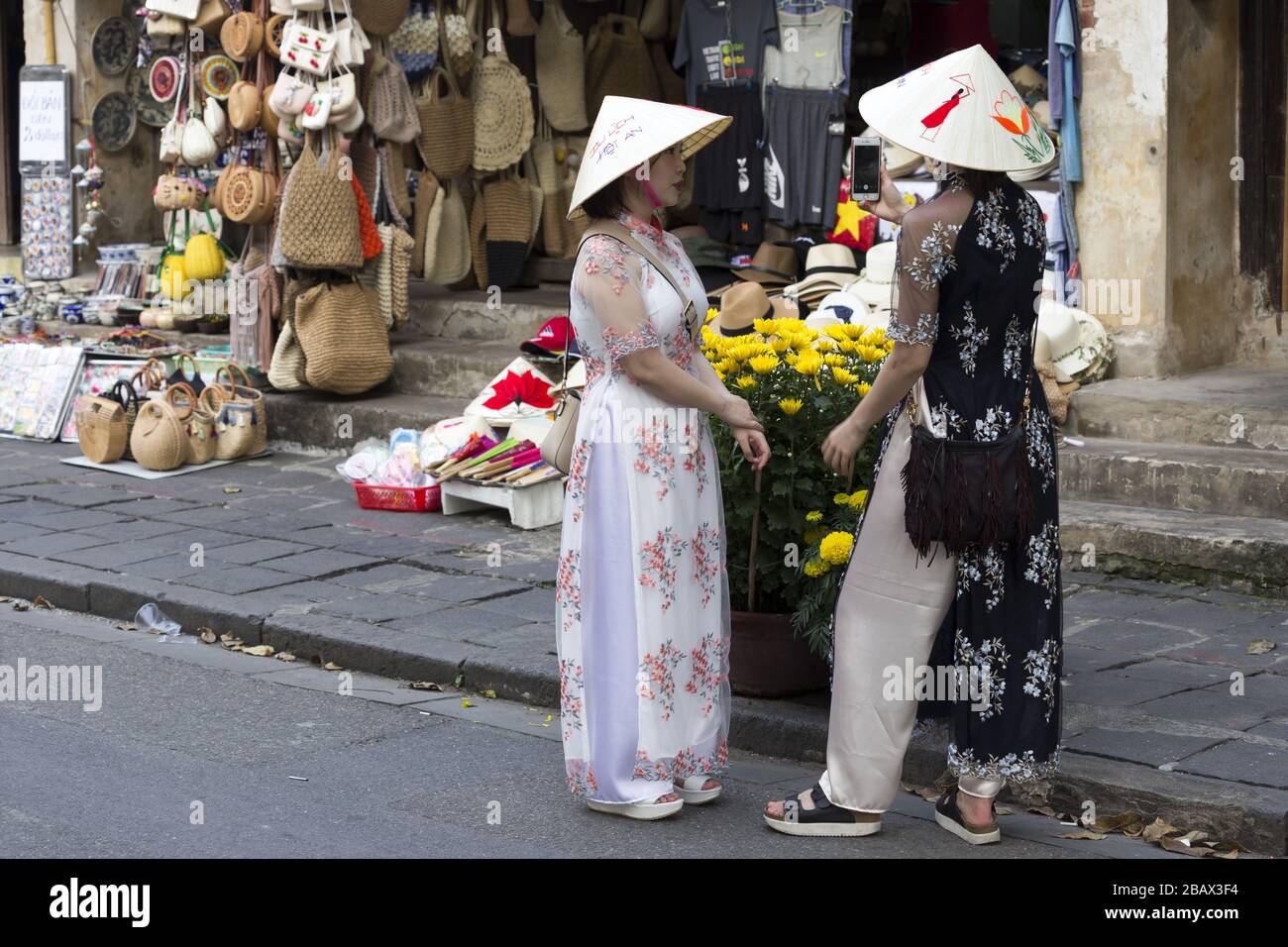 Deux filles vietnamiennes vêtues de vêtements ethniques traditionnels et portant des chapeaux de cône debout sur Hoi an Street pendant la célébration du nouvel an chinois asiatique Banque D'Images