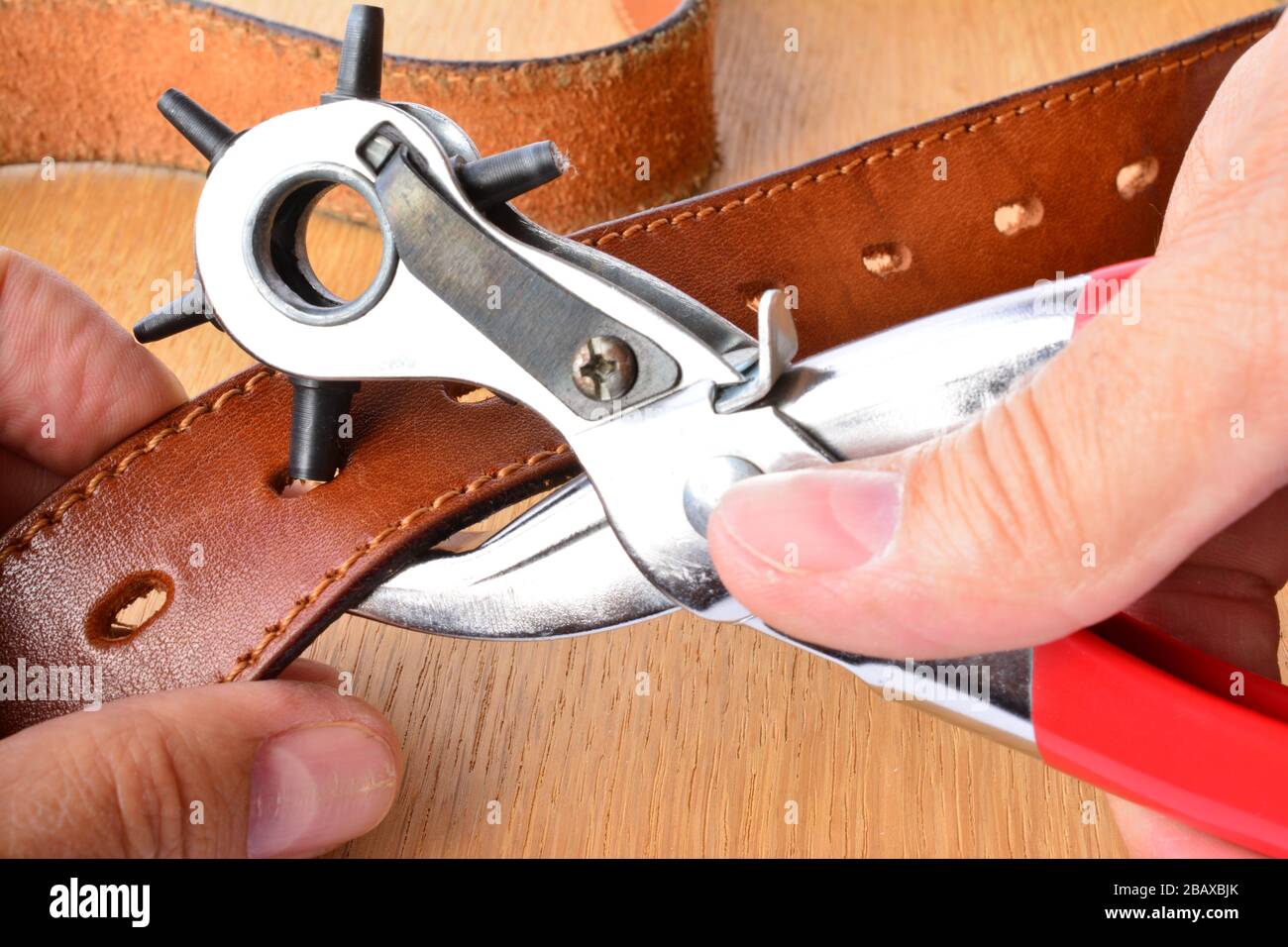 Perforation de ceinture en cuir, outil de perforation et nouvelle ceinture en cuir dans les mains de l'artisan sur fond en bois Banque D'Images