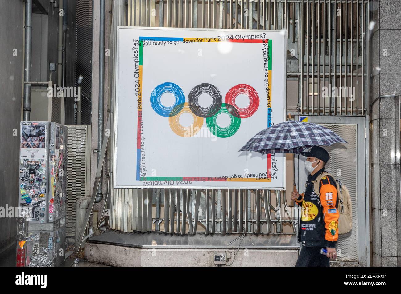 Un homme qui tient un parapluie marche par une affiche olympique 2024 pendant la pandémie du virus corona. Le gouvernement métropolitain de Tokyo a demandé aux résidents de rester chez eux ce week-end comme mesure préventive contre une poussée de nouvelles infections de cas de Coronavirus (COVID-19). Banque D'Images