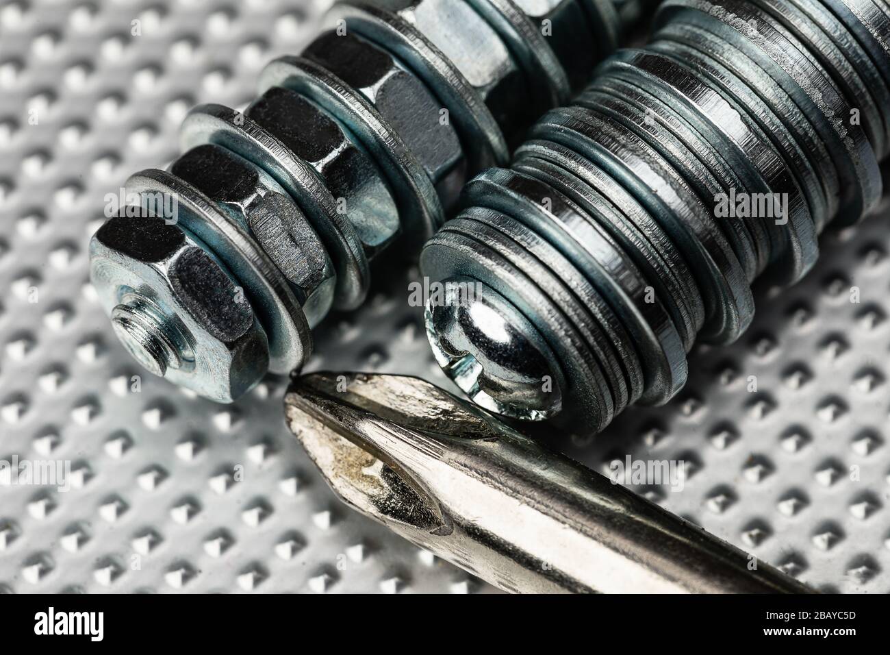 macro de petits boulons à tons bleus frais avec écrous et rondelles sur une surface en acier industriel avec le dessus d'un tournevis cruciforme. Contraste élevé Banque D'Images