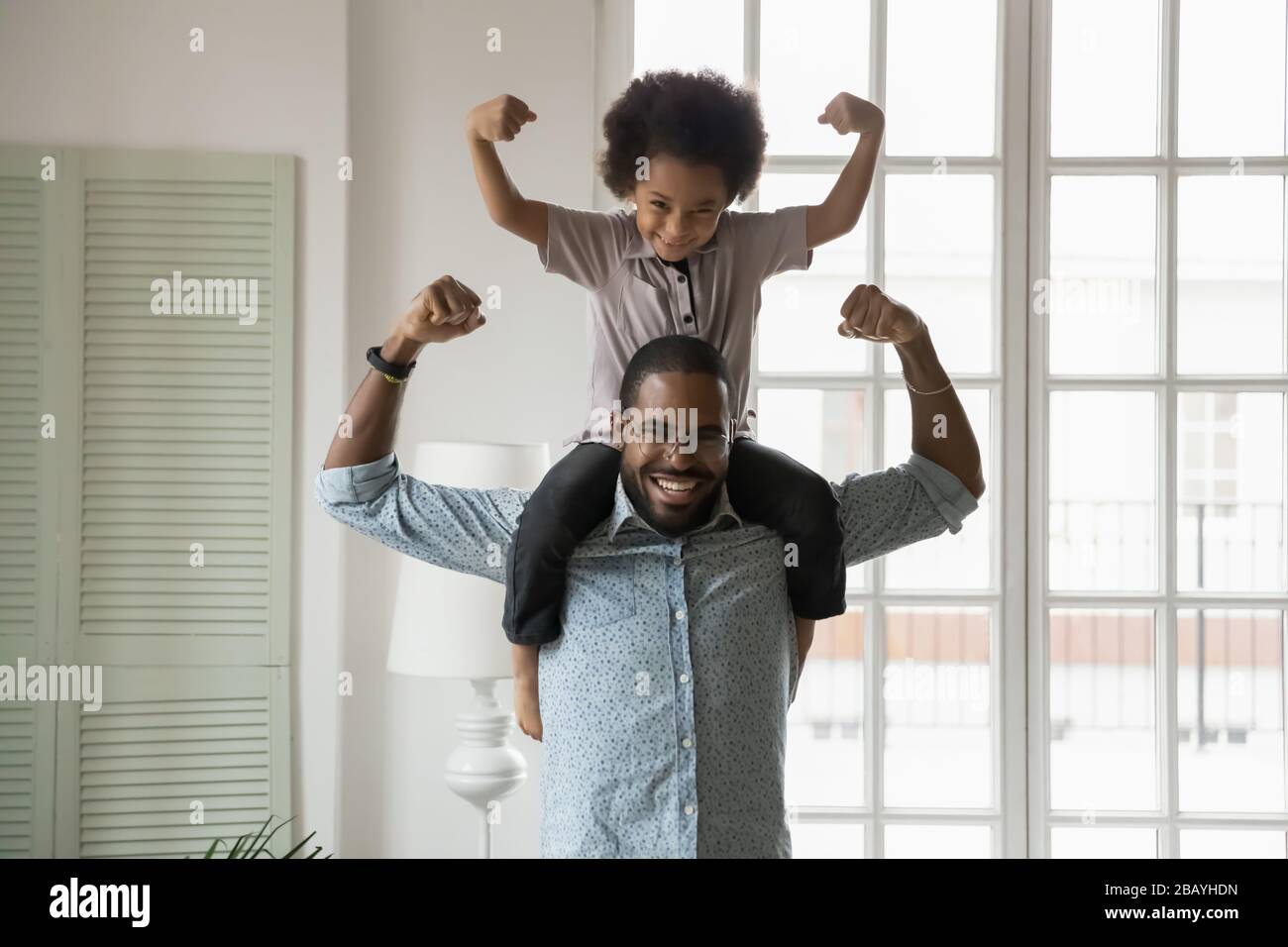 Ethnicité africaine petit fils assis sur les épaules des pères montrant des biceps Banque D'Images