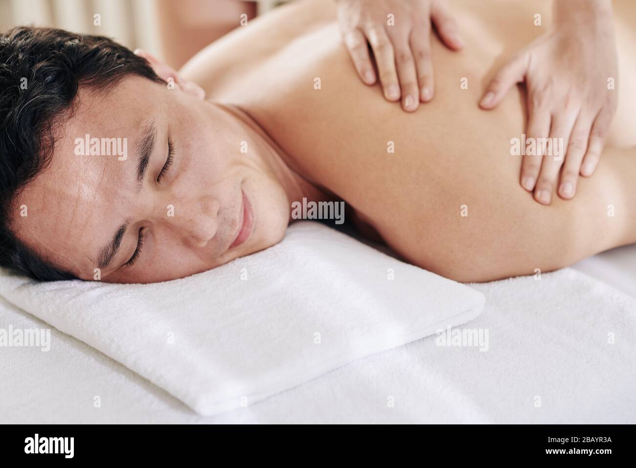 Un homme souriant et bien souriant qui profite d'un massage des épaules et du dos en tissu profond dans le salon de spa Banque D'Images